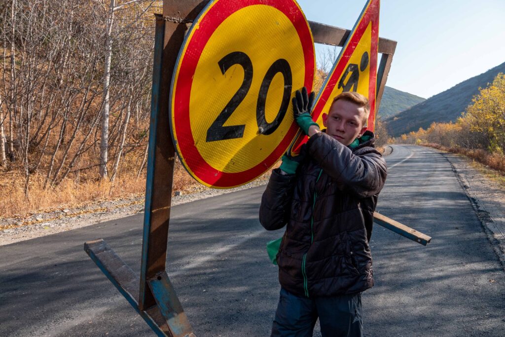 Trabajador sostiene señal de tráfico de límite de velocidad 20 km/h en carretera de montaña, ilustrando la importancia de la seguridad vial y el respeto a las normas de circulación.