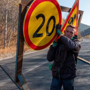 Trabajador sostiene señal de tráfico de límite de velocidad 20 km/h en carretera de montaña, ilustrando la importancia de la seguridad vial y el respeto a las normas de circulación.